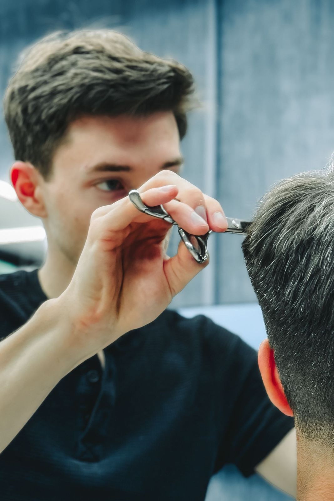 Barbeiro aparando o cabelo na tesoura, cliente refletido no espelho